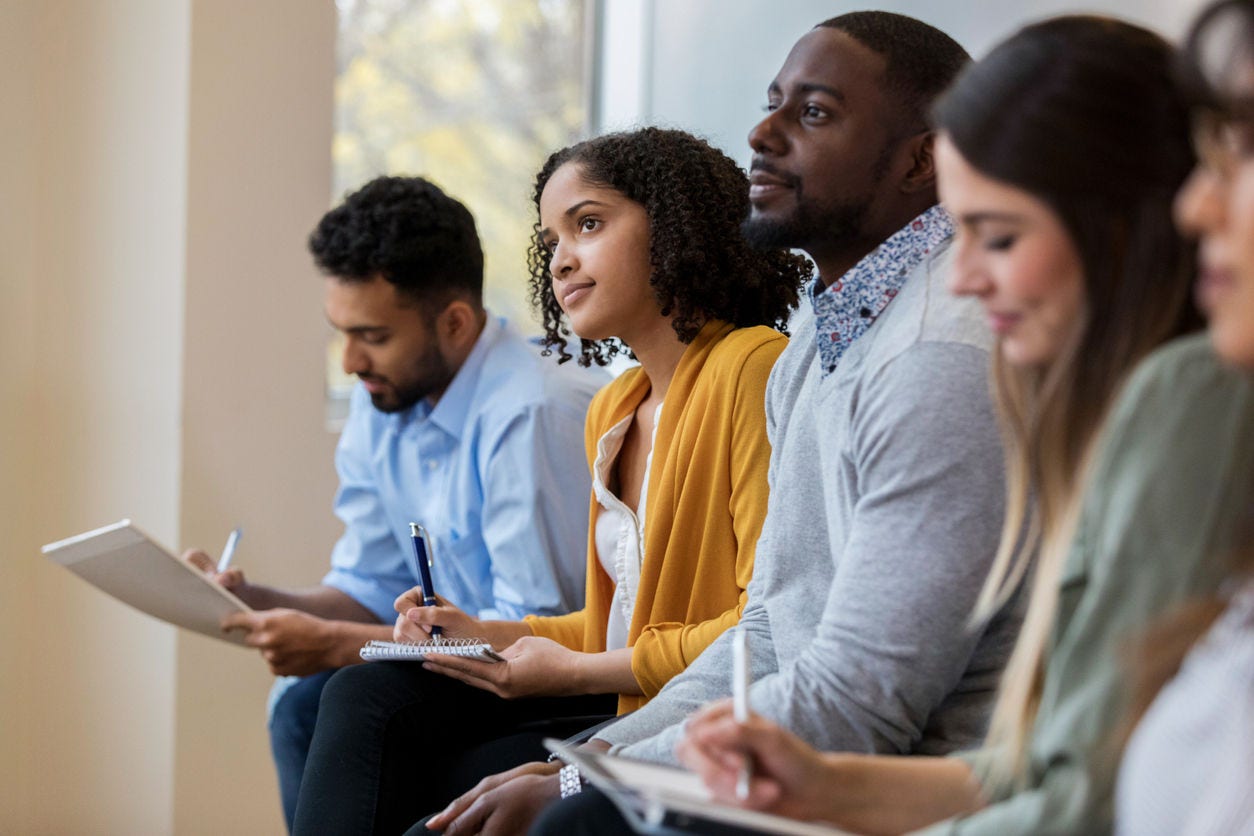 1132123971 A group of business people sit in a row in a training class. They look at an unseen speaker as they concentrate on his lecture.